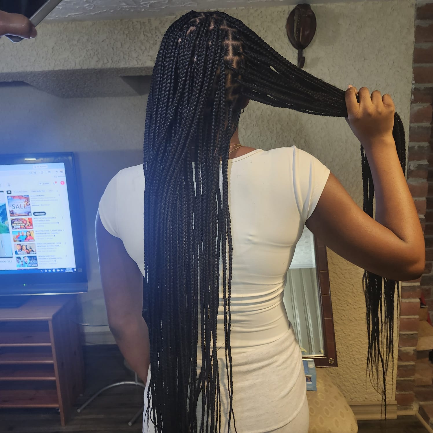 Client holding a section of waist-length knotless braids in warm light